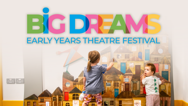Two young children play in front of a wall of wooden houses. Text: Big Dreams Early Years Theatre Festival 