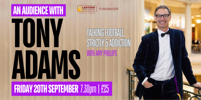 Photo of a smiling Tony Adams in a dark blue velvet suit and bow tie leaning on a fancy balustrade in front of a posh cream and gold interior.