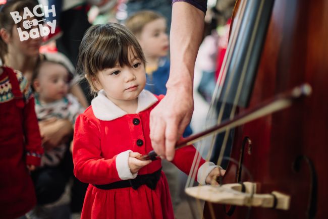 festive toddler inspects cello